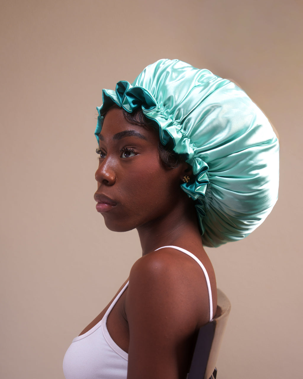 Woman wearing a teal satin bonnet against a beige background