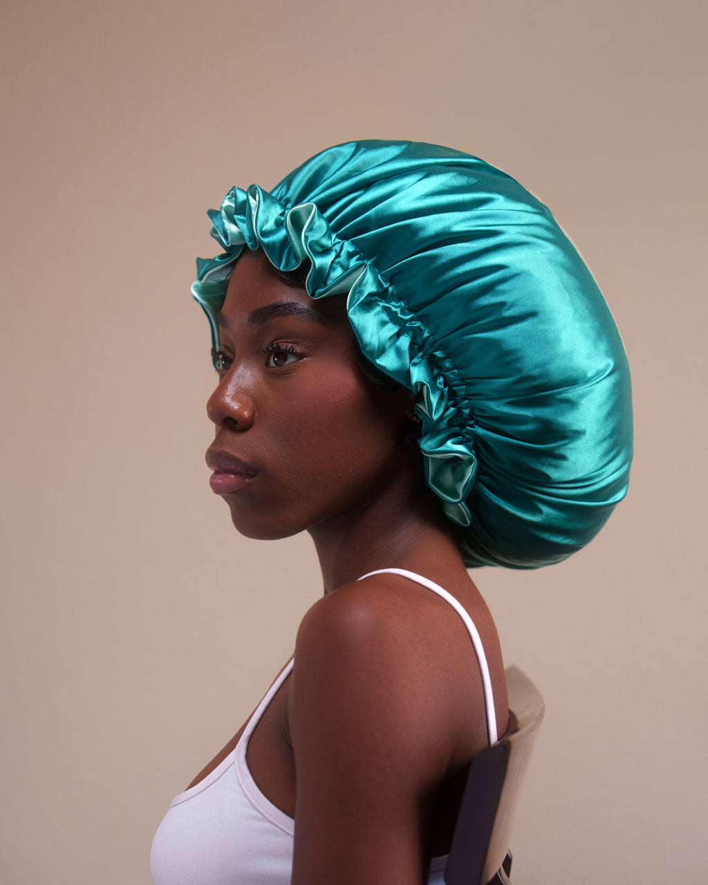 Woman wearing a teal satin bonnet against a beige background