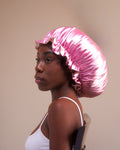 Woman wearing a pink satin hair bonnet against a beige background