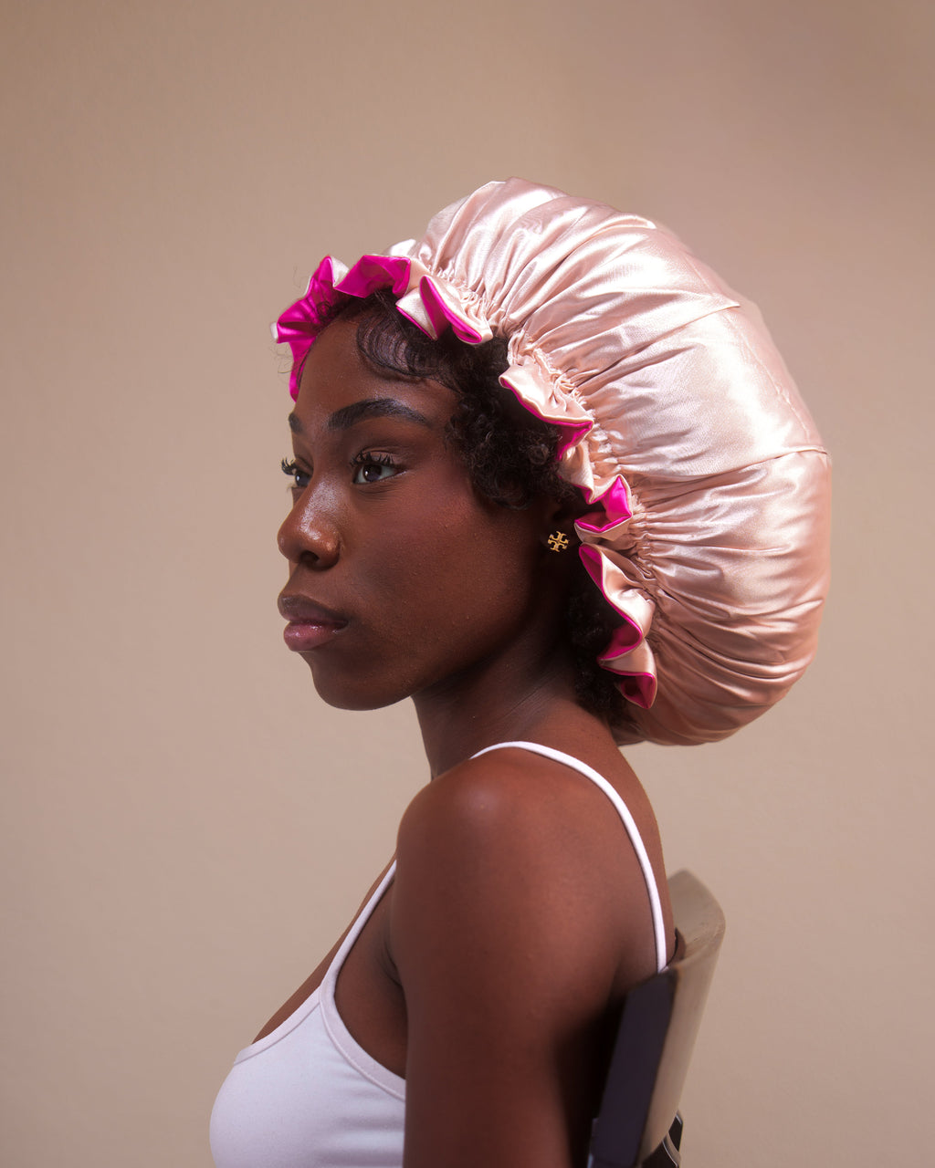 Woman wearing a beige and pinksatin hair bonnet on a beige background