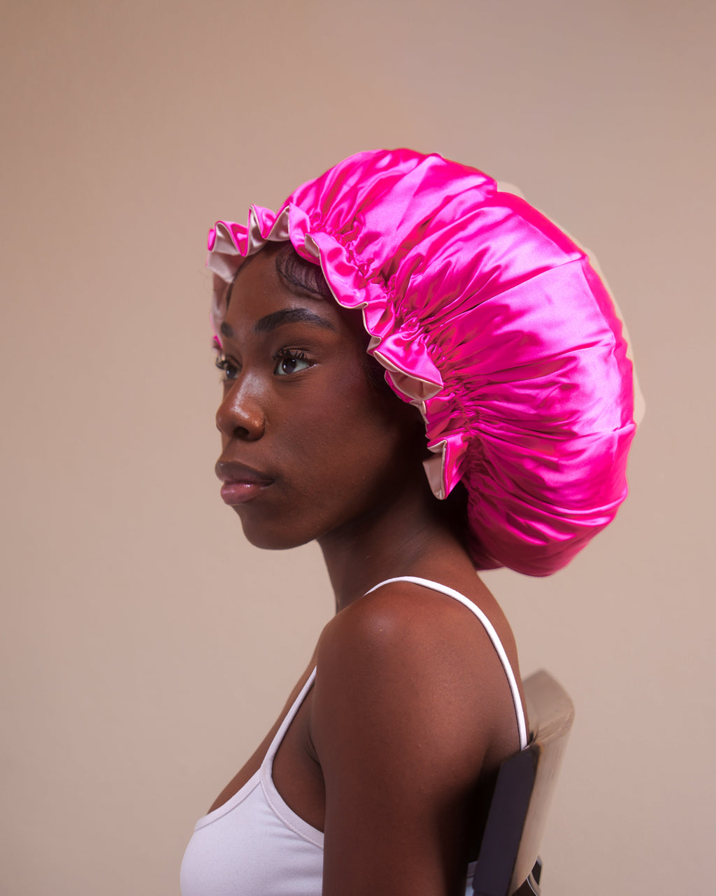 Woman wearing a bright pink satin bonnet against a beige background