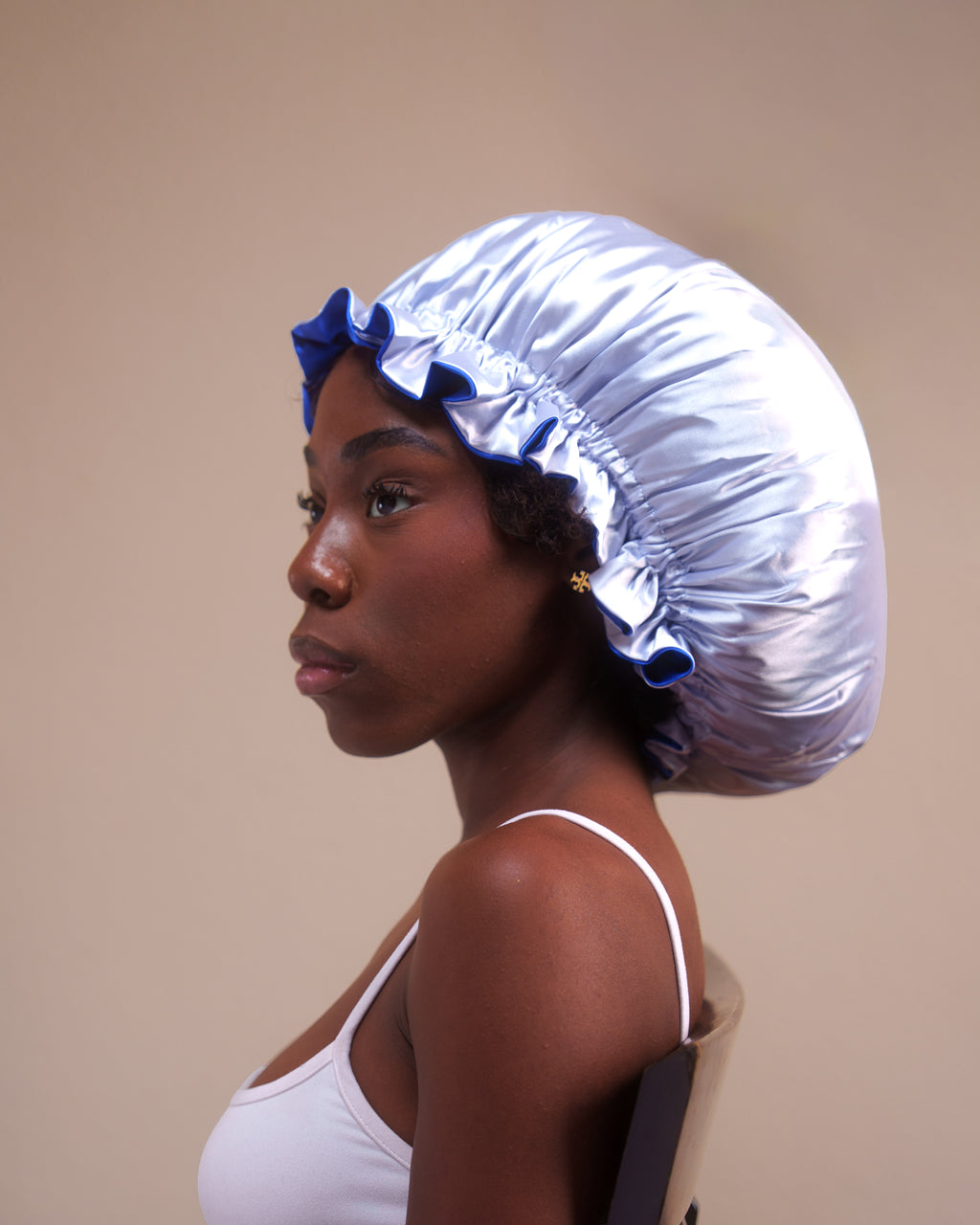 Woman wearing a large blue satin hair bonnet against a beige background